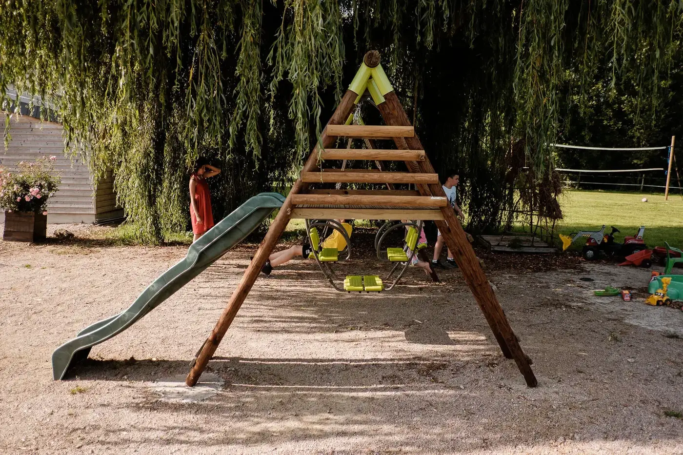 Aire de jeux pour enfants avec toboggan sous un saule pleureur